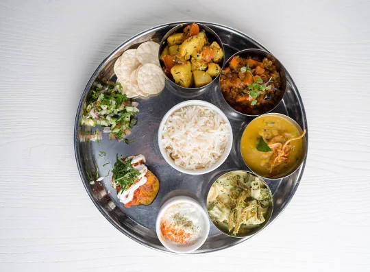 Vegetarian thali with rice, sabzis and raita, served in steel bowls